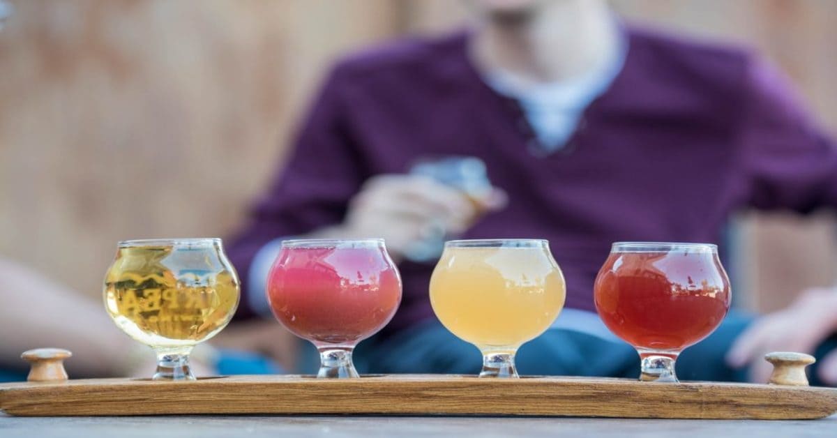 A wooden flight with four different craft beer samples in small glasses.