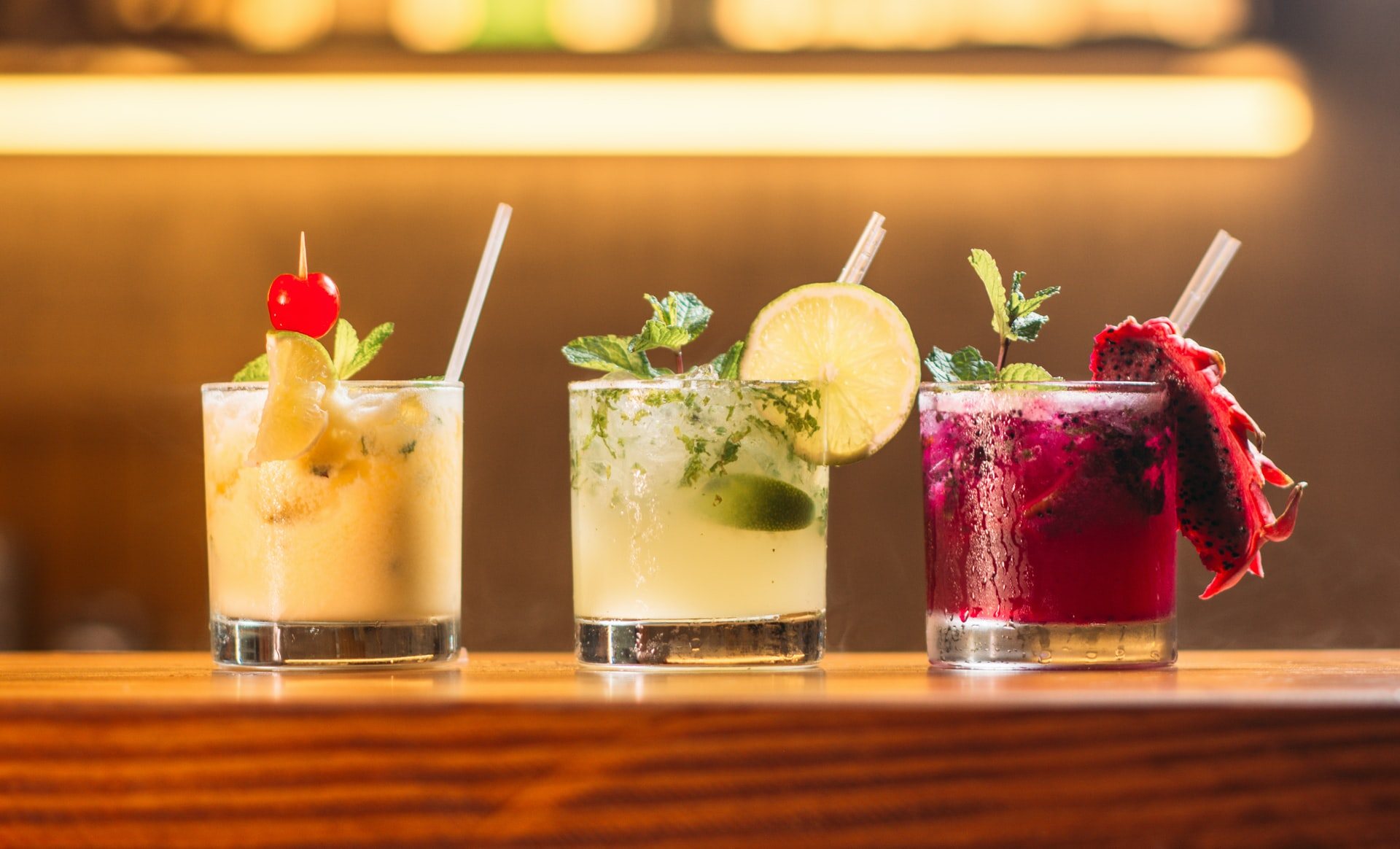 Three colorful cocktails with garnishes on a wooden bar