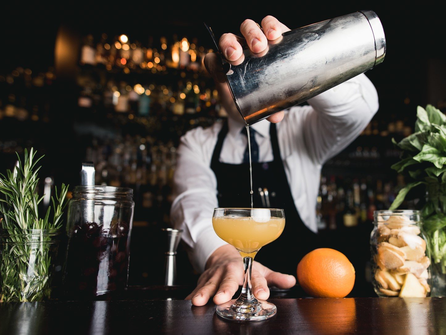 Bartender shaking cocktail with various garnishes visible
