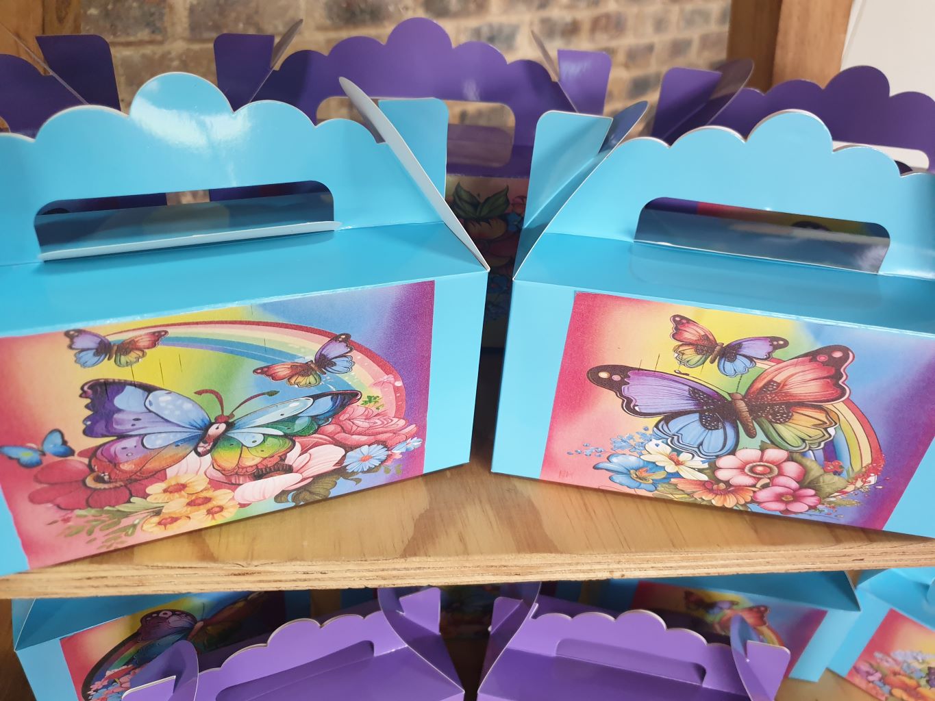 Colorful butterfly-themed party favour boxes stacked on a shelf.
