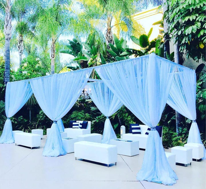 Outdoor canopy with light blue drapes and white lounge furniture.