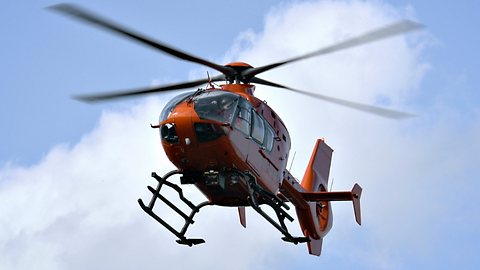 Orange helicopter flying against a blue sky