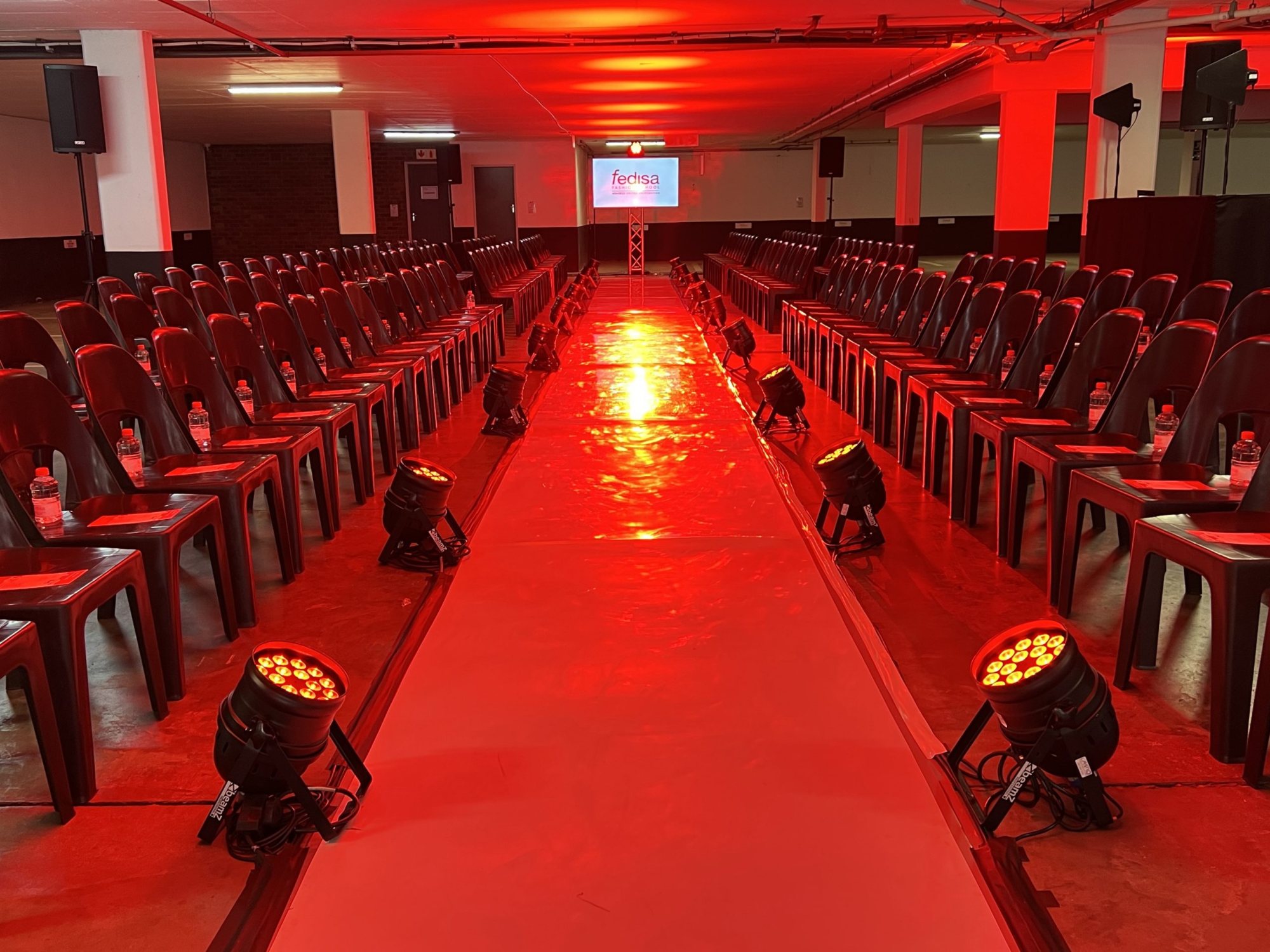 Runway setup with red lighting and black chairs in a venue