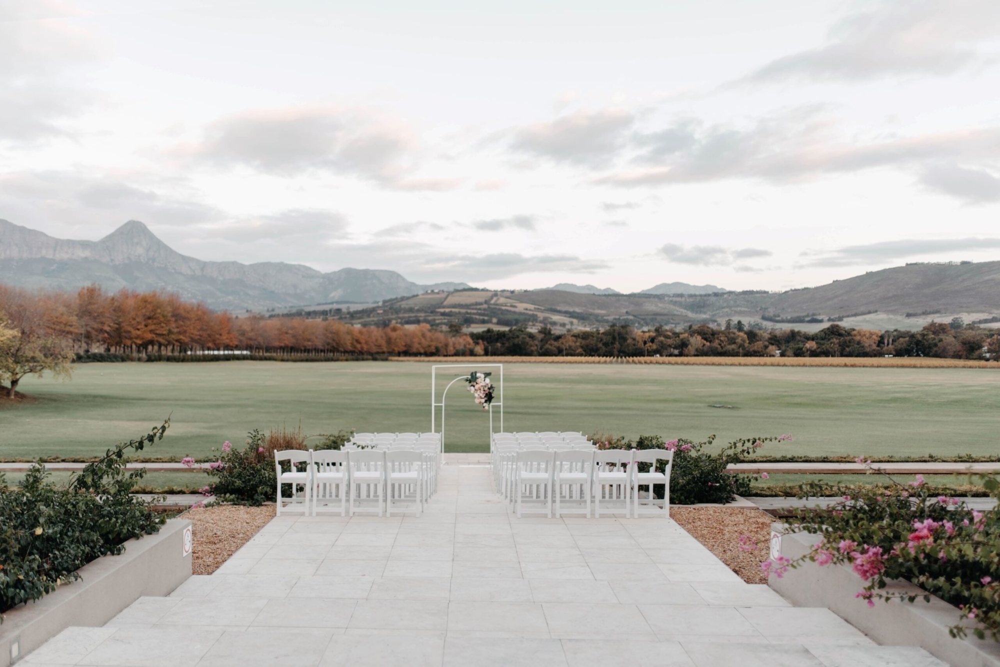 Outdoor ceremony setup with white chairs and mountain backdrop