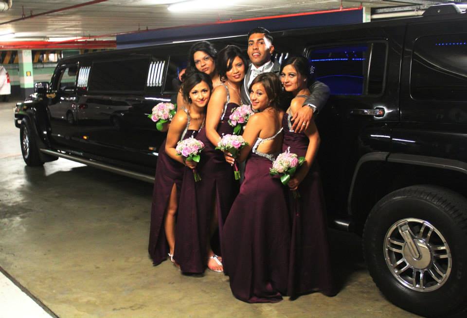 Group of people posing next to a stretch Hummer limousine.