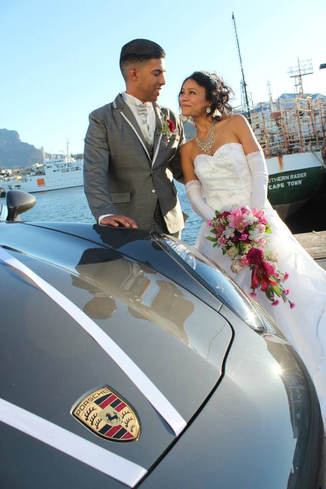 A couple in wedding attire beside a Porsche in Cape Town.