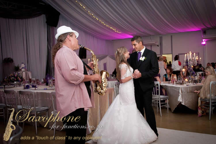 Saxophonist performing at a wedding reception with a couple dancing.