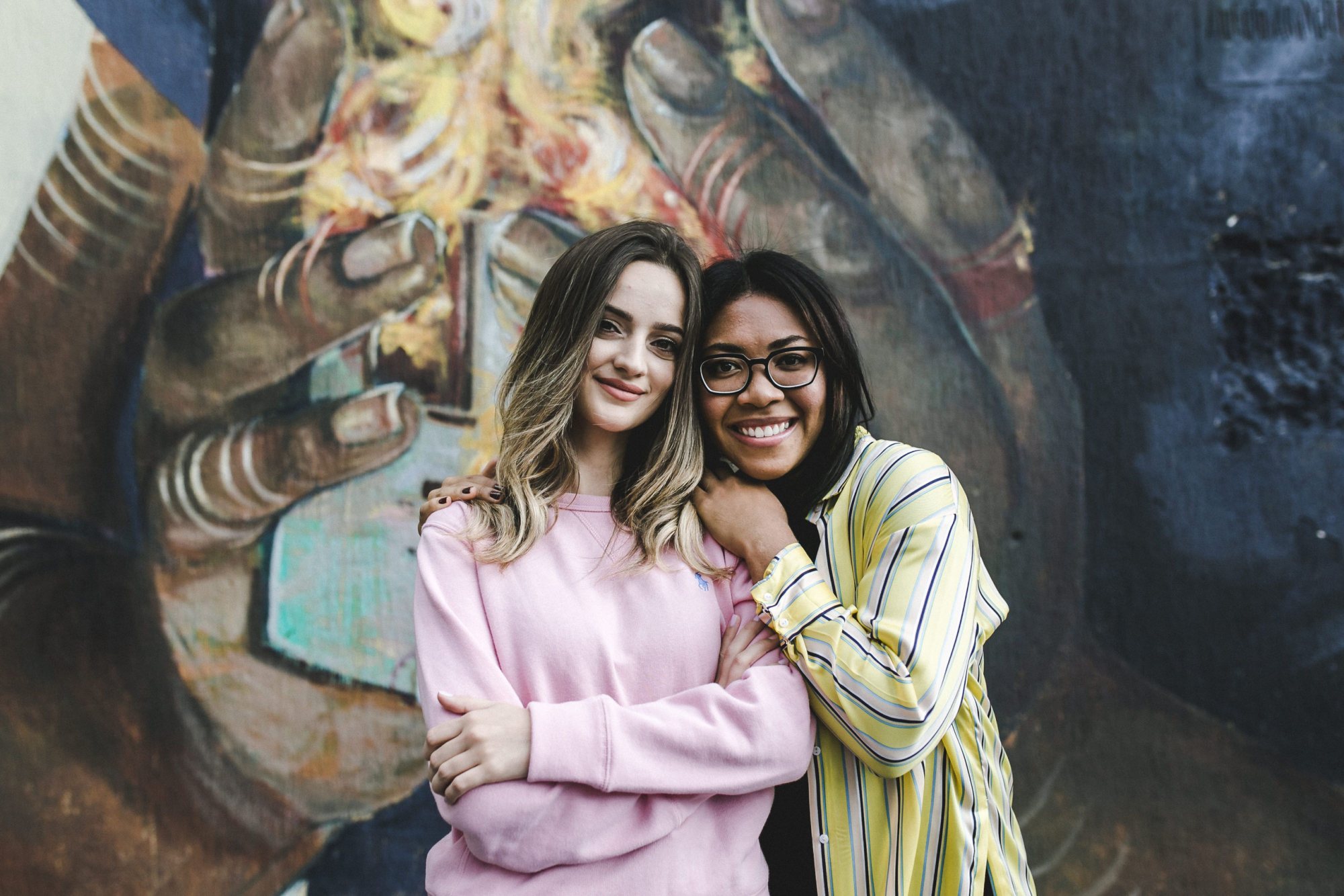Two friends posing in front of a colorful mural.