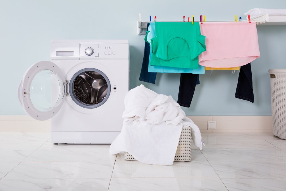 Washing machine with open door and clothes drying on rack.