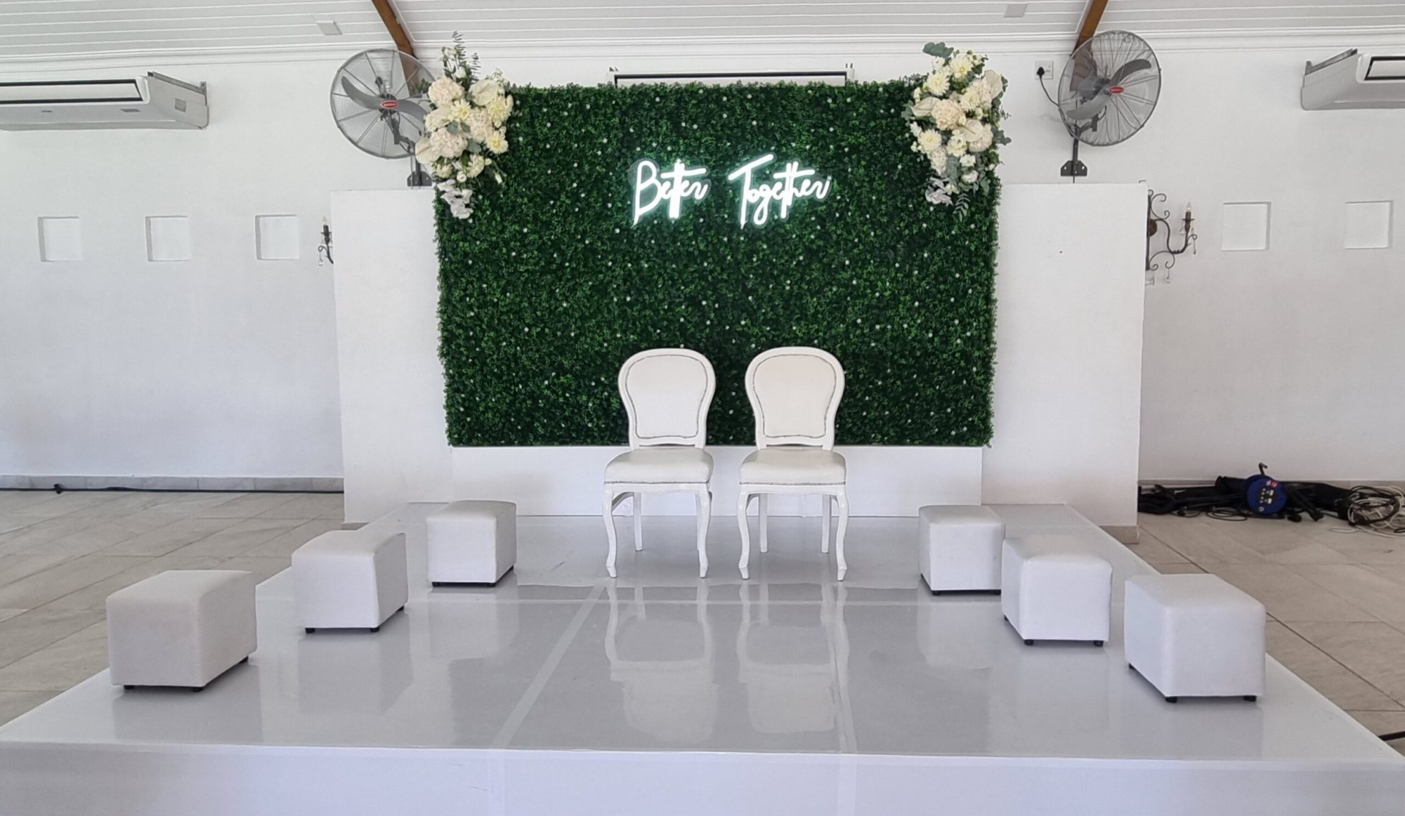 Ceremony setup with green wall, flowers, and white seating