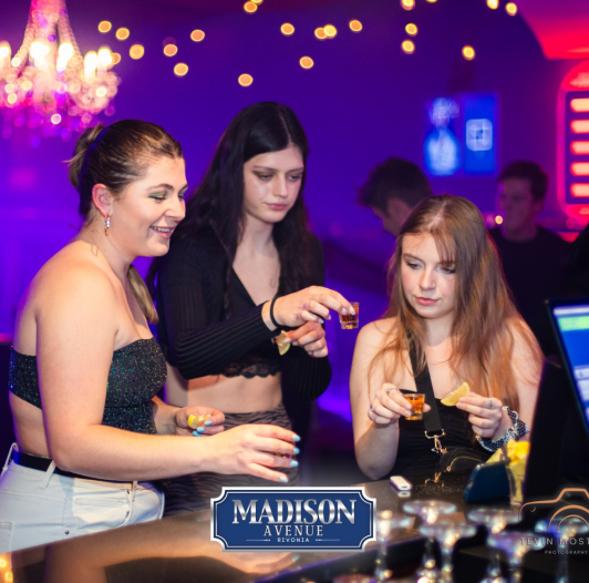 Three guests enjoying drinks at the bar in a nightclub setting.