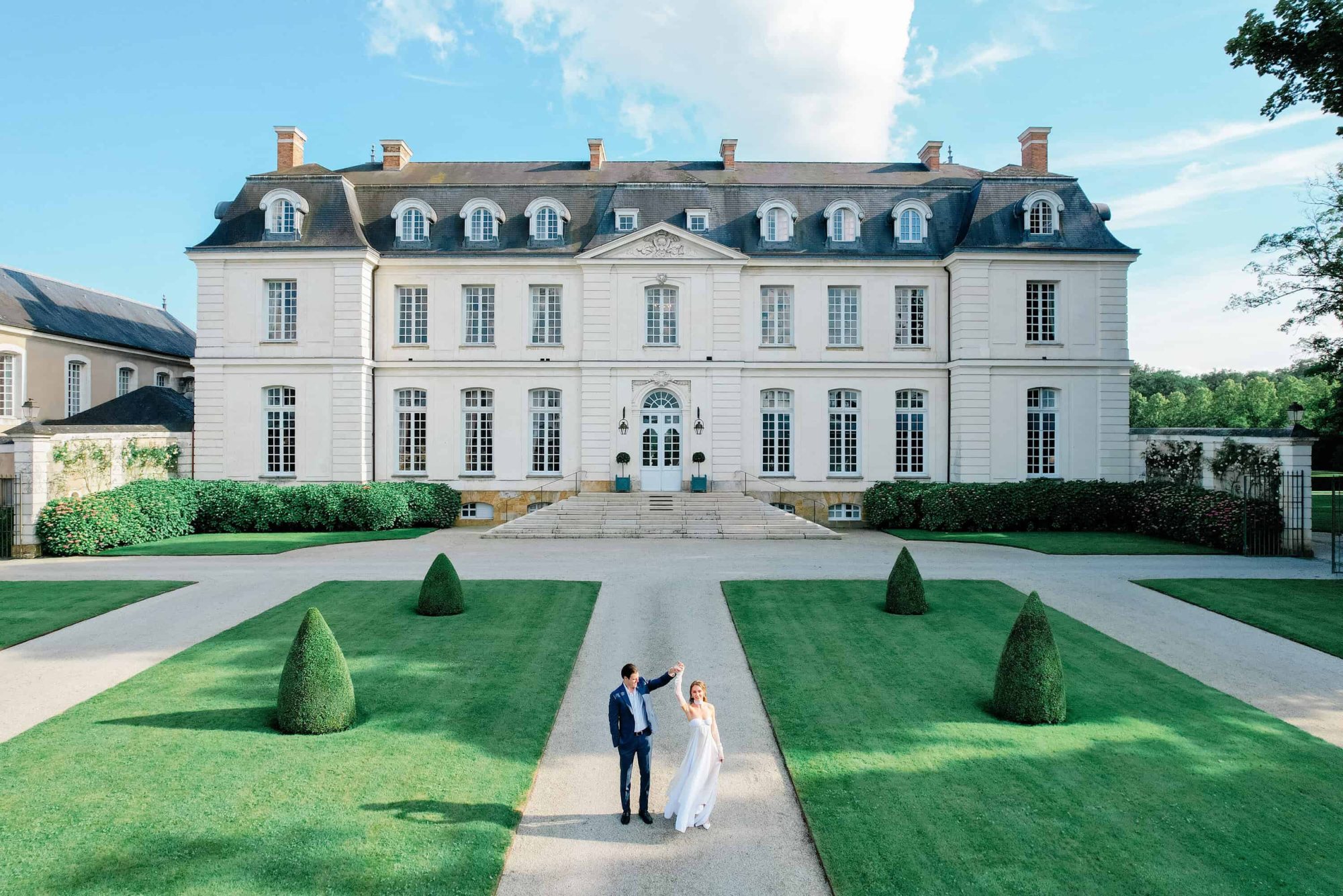 Front view of a grand wedding venue with a couple dancing in the garden.