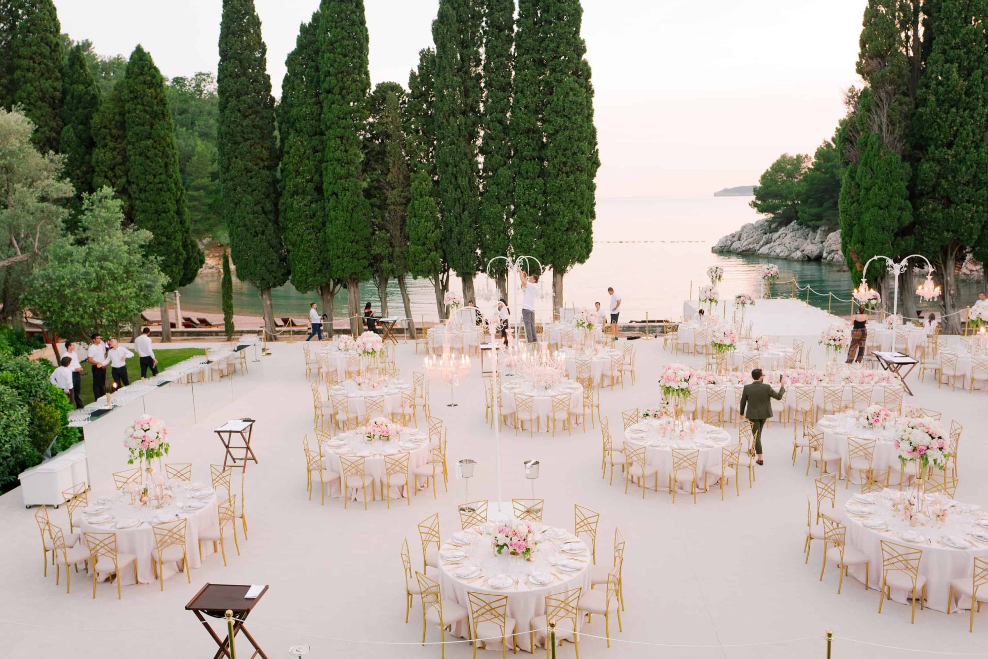 Outdoor wedding setup with round tables and floral centerpieces near a lake