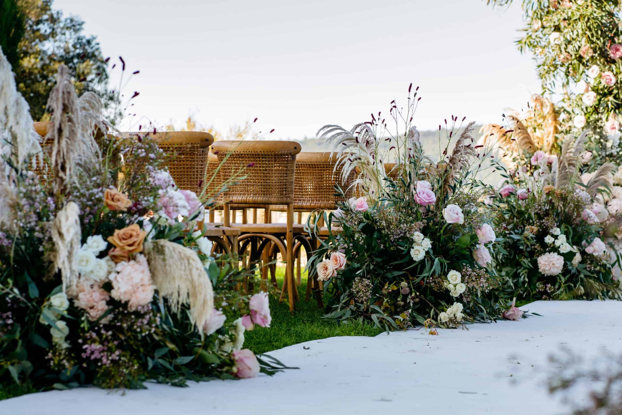 Floral arrangements beside elegant chairs for a wedding ceremony.