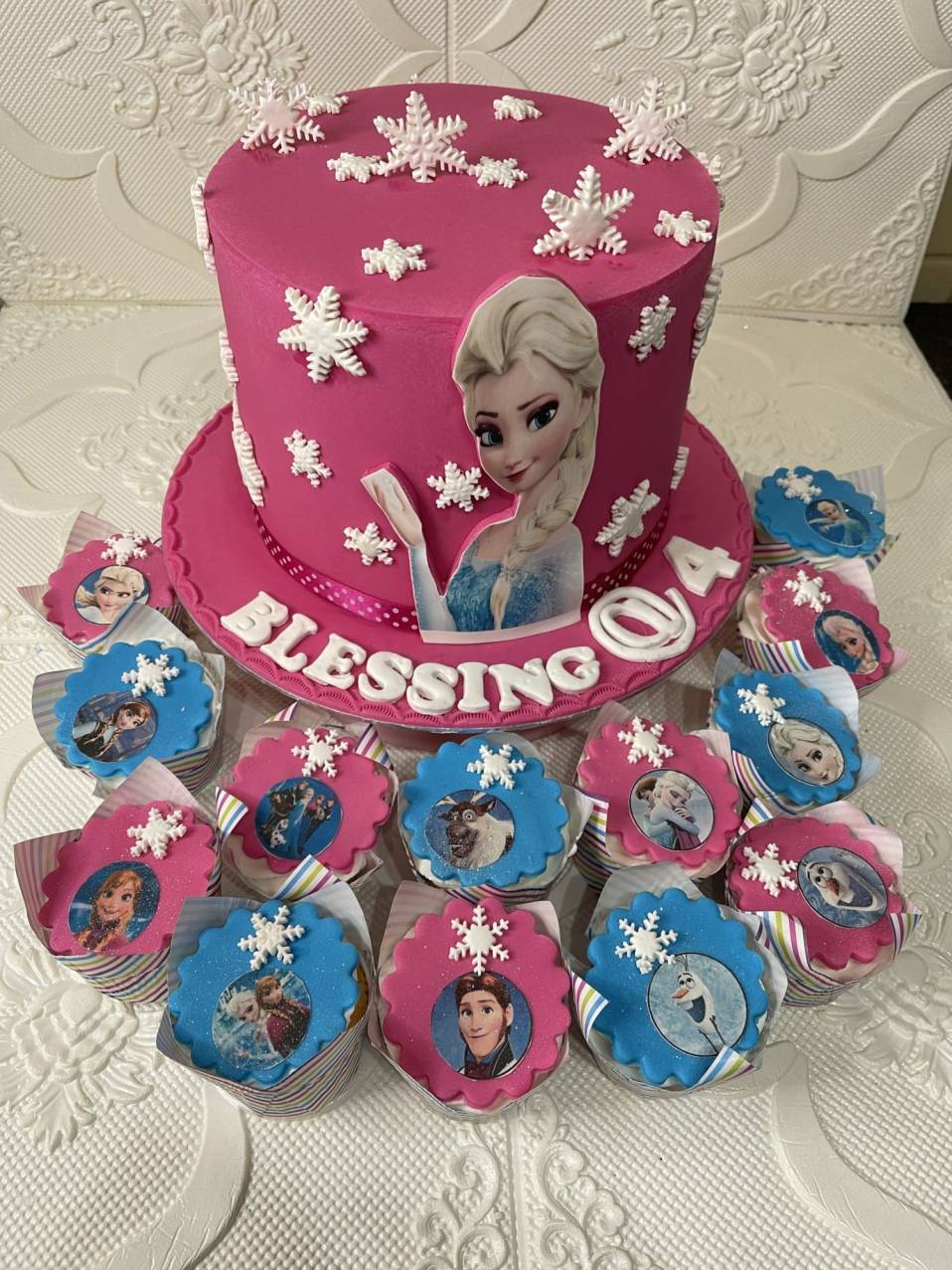 Pink Frozen-themed birthday cake with snowflakes and character cupcakes.
