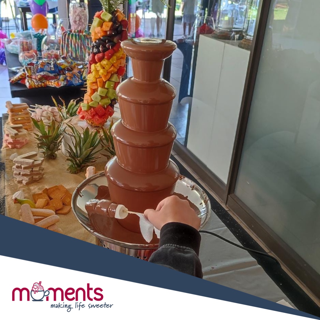 Multi-tiered chocolate fountain with fruits arranged around it