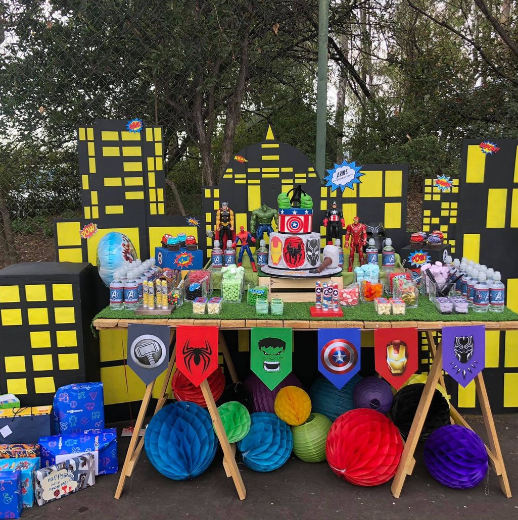 Superhero themed party decor with cake and treats.