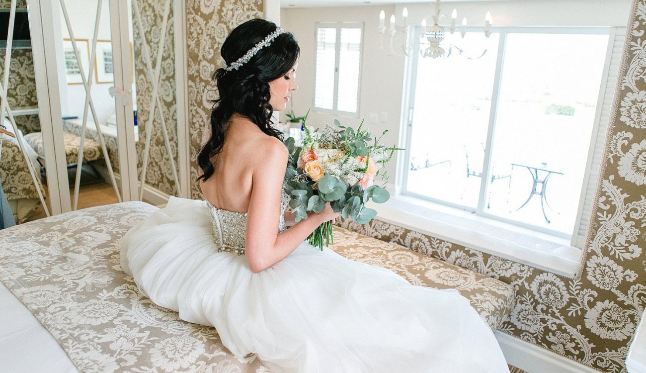 Bride holding a floral bouquet while seated in a decorated room.