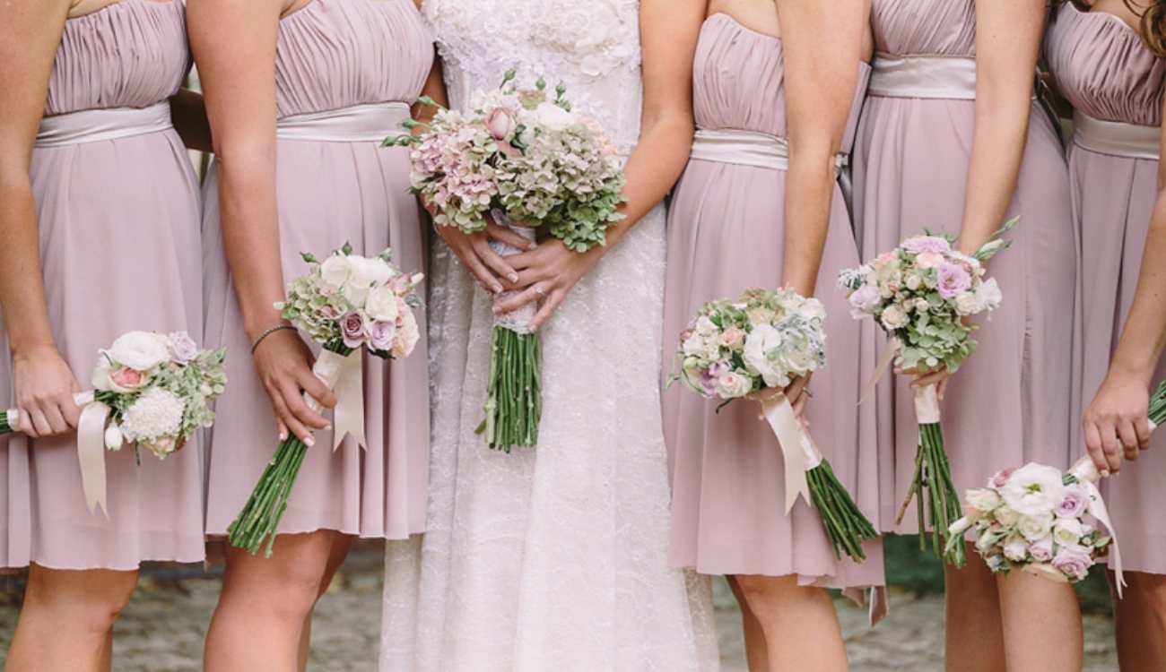 Group of bridesmaids holding floral bouquets in soft pink dresses