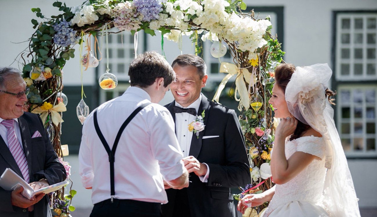 Couple exchanging vows under a floral arch at an outdoor ceremony.