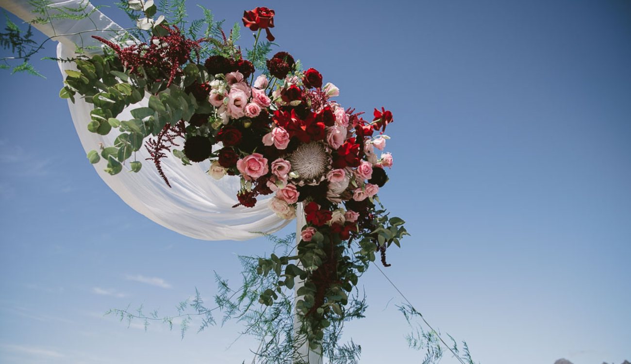 Floral arch adorned with red and pink roses under a clear blue sky