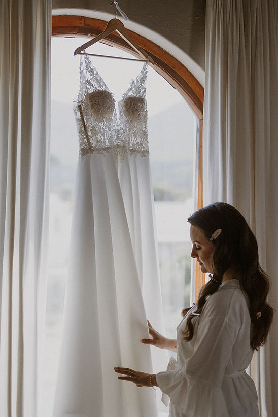 Bridal gown hanging by a window with a woman admiring it