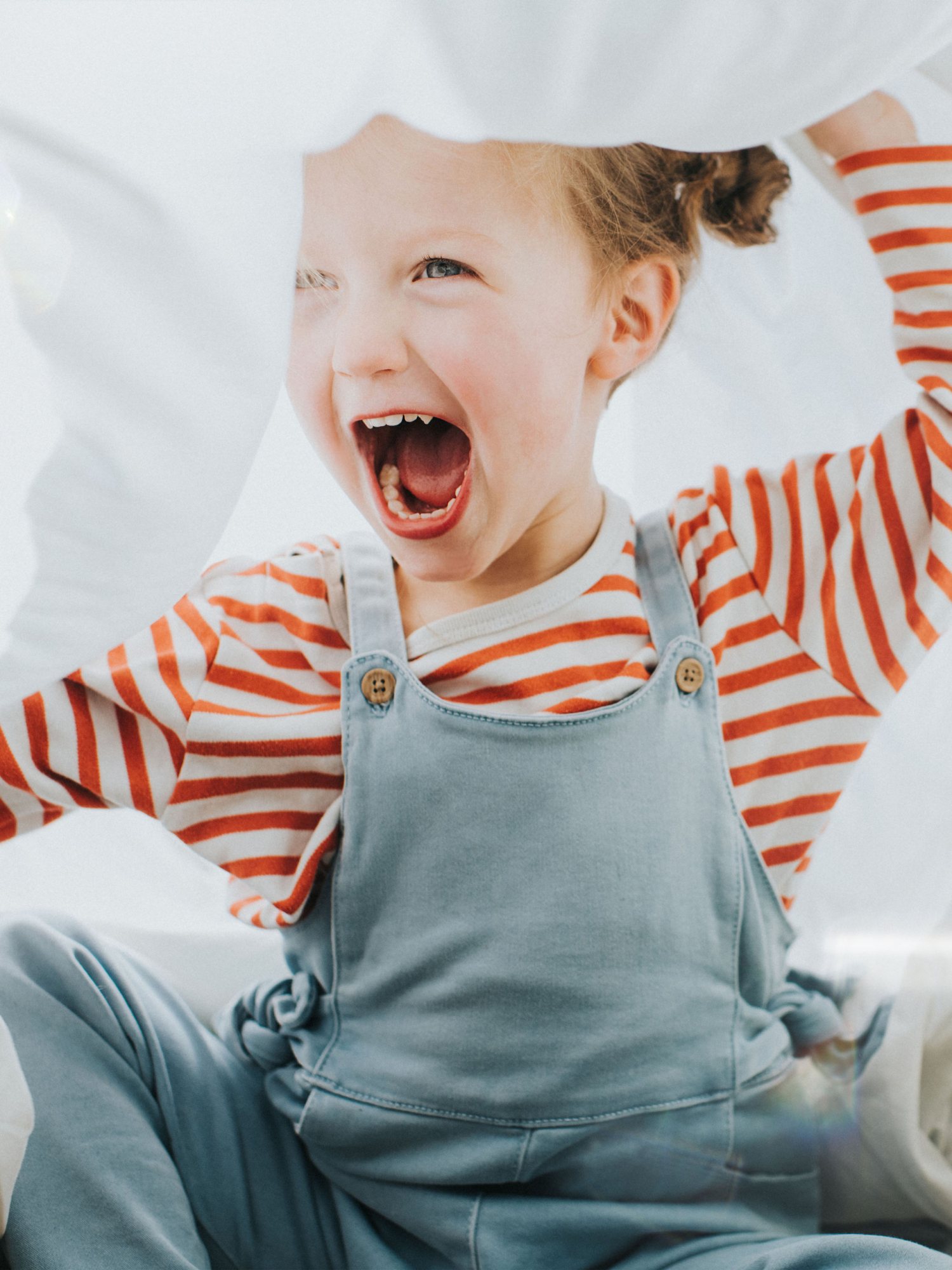Child laughing and playing, wearing a striped shirt and overalls.