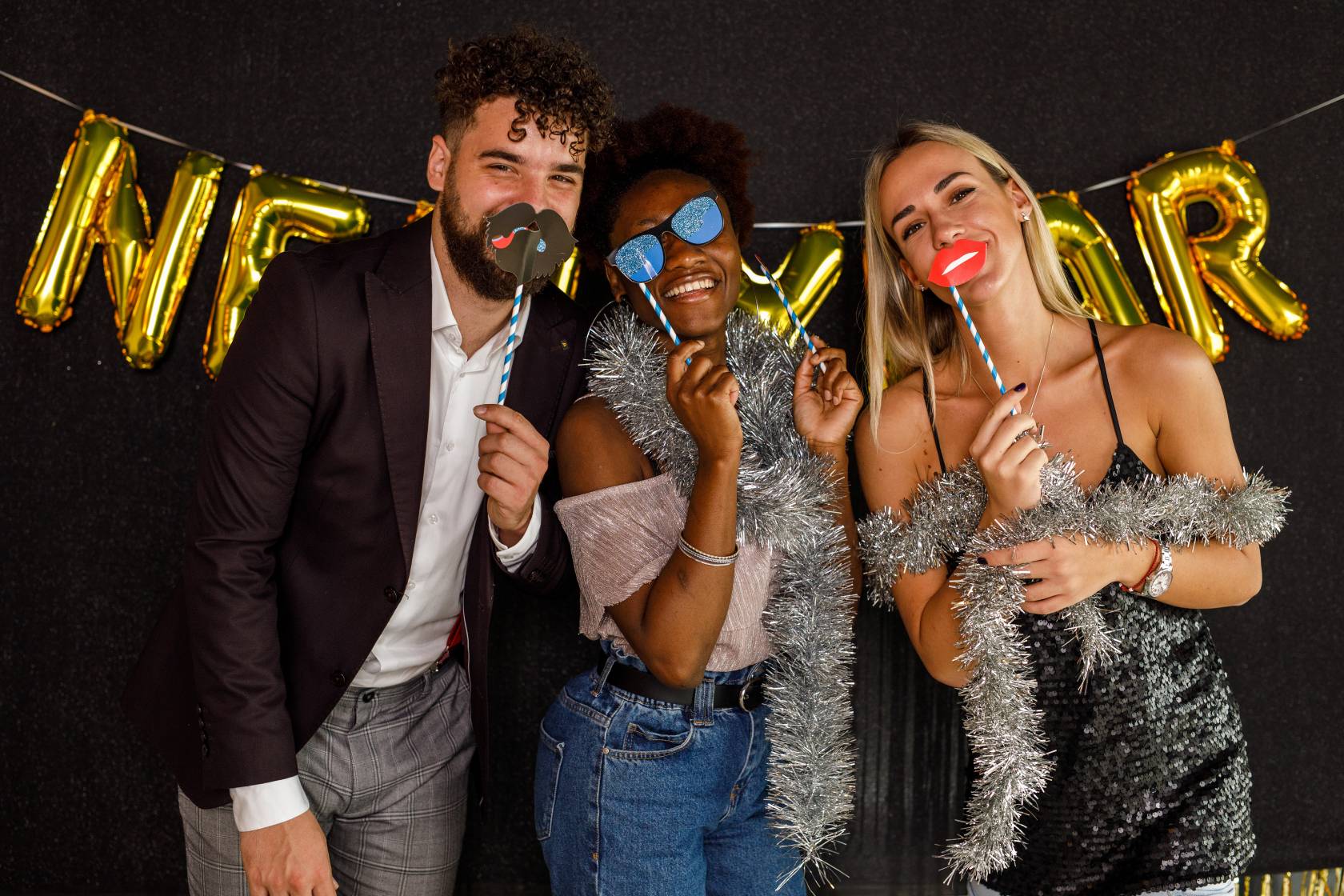 Three people smiling with photo props in front of a festive backdrop