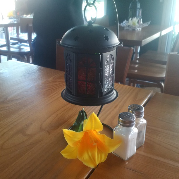 Hanging black lantern with a yellow flower on a wooden table.