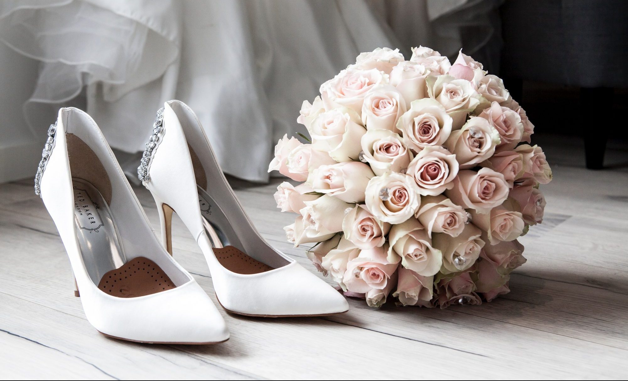 White bridal shoes next to a bouquet of pink roses