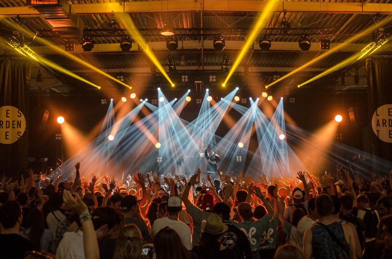 A crowd at a concert with raised hands and colorful stage lights.