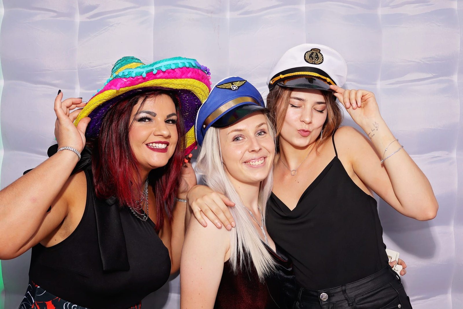 Three women with hats posing in a photo booth