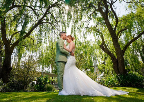 Couple embracing under willow trees at a wedding venue