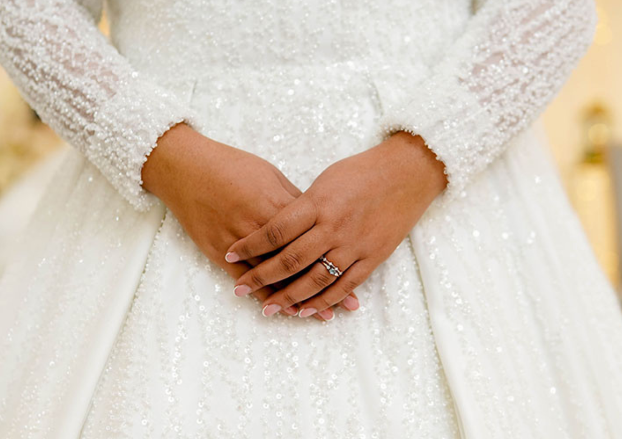 Close-up of a bride's hands with a detailed wedding gown and ring