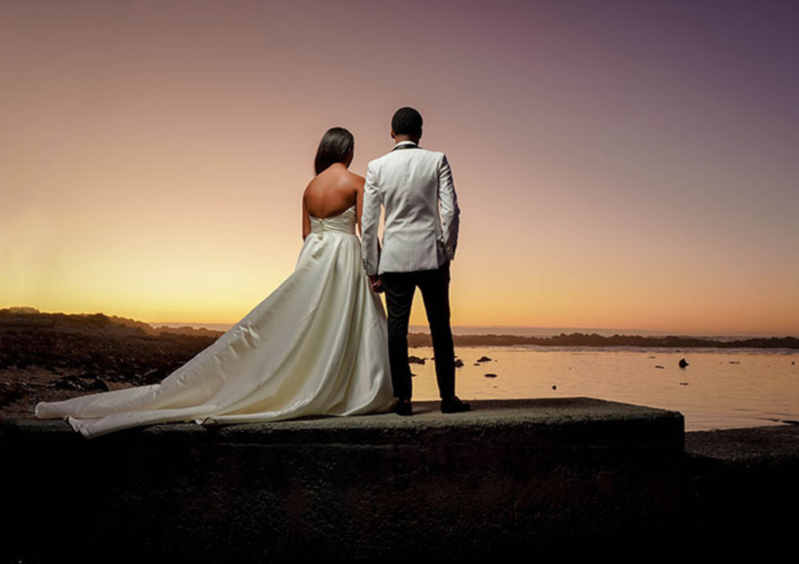 Bride and groom holding hands at sunset by the ocean.