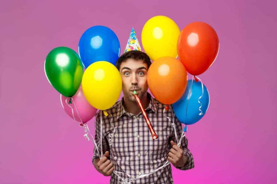 Person holding colorful balloons and wearing a party hat.