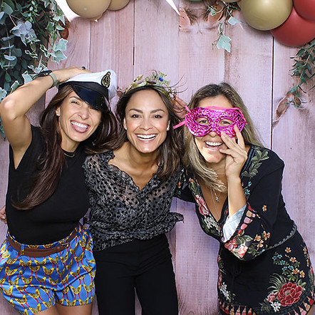 Three women in a photo booth with props and a festive backdrop.