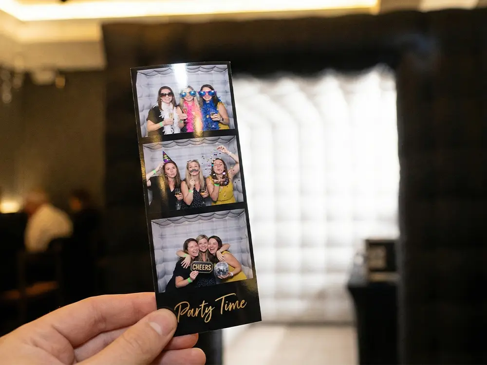 Hand holding a photo booth print strip with four images of guests.