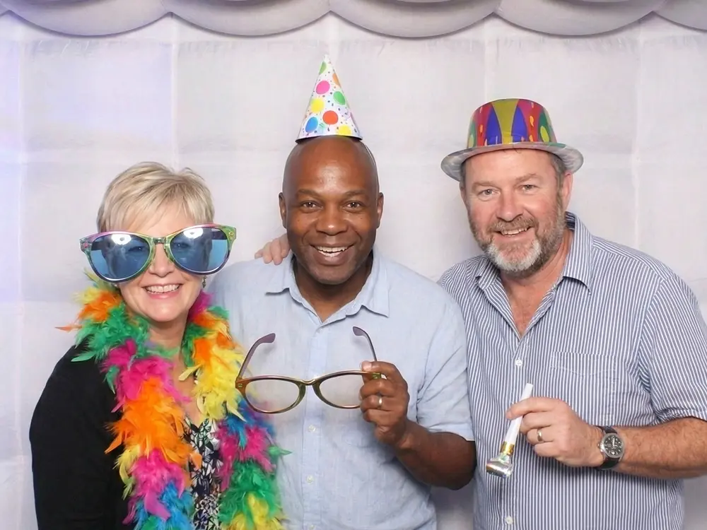 Three guests in a photo booth wearing party props.