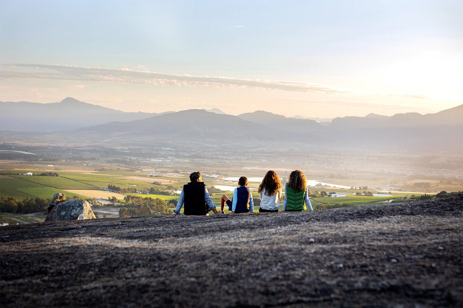 People sitting on a rock overlooking the vineyards at sunset.