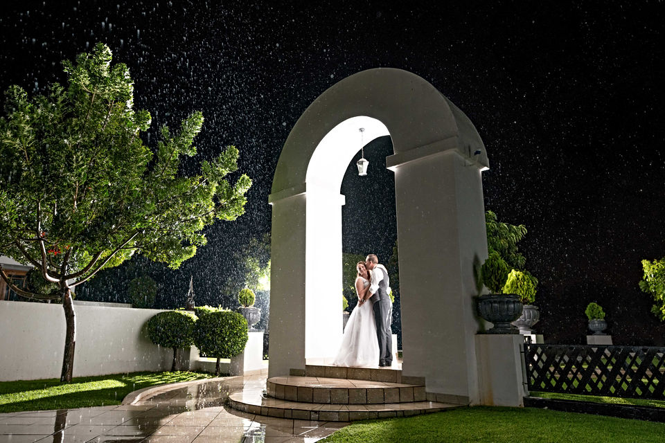 Couple standing under an arch in pouring rain at night
