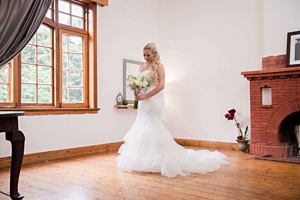 Bride in wedding dress holding bouquet in a well-lit room.