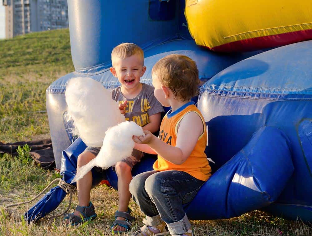 Two children playing near a soft play area while holding cotton candy.