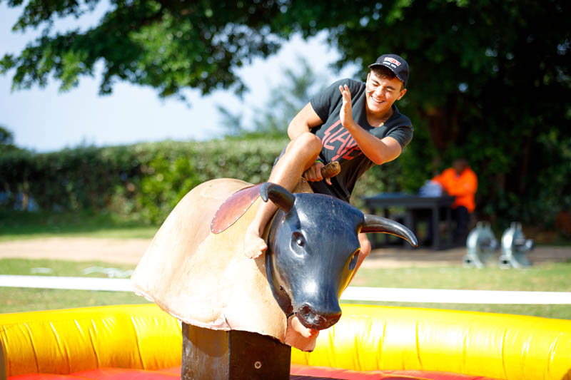 Young man riding a mechanical bull in an inflatable arena.