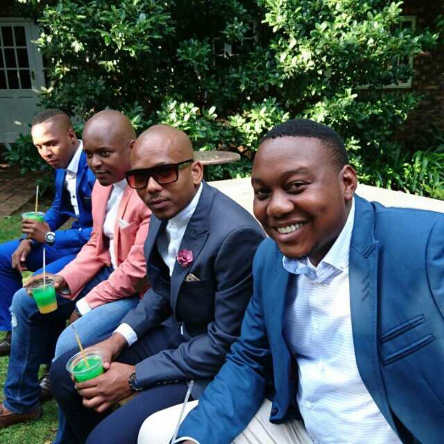 Four men in suits sitting outdoors with colorful cocktails.