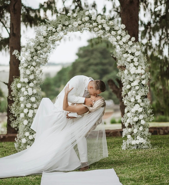 Couple kissing under a floral wedding arch outdoors