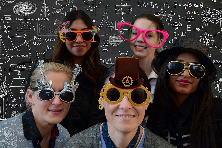 Group of five people with oversized glasses in front of a chalkboard.