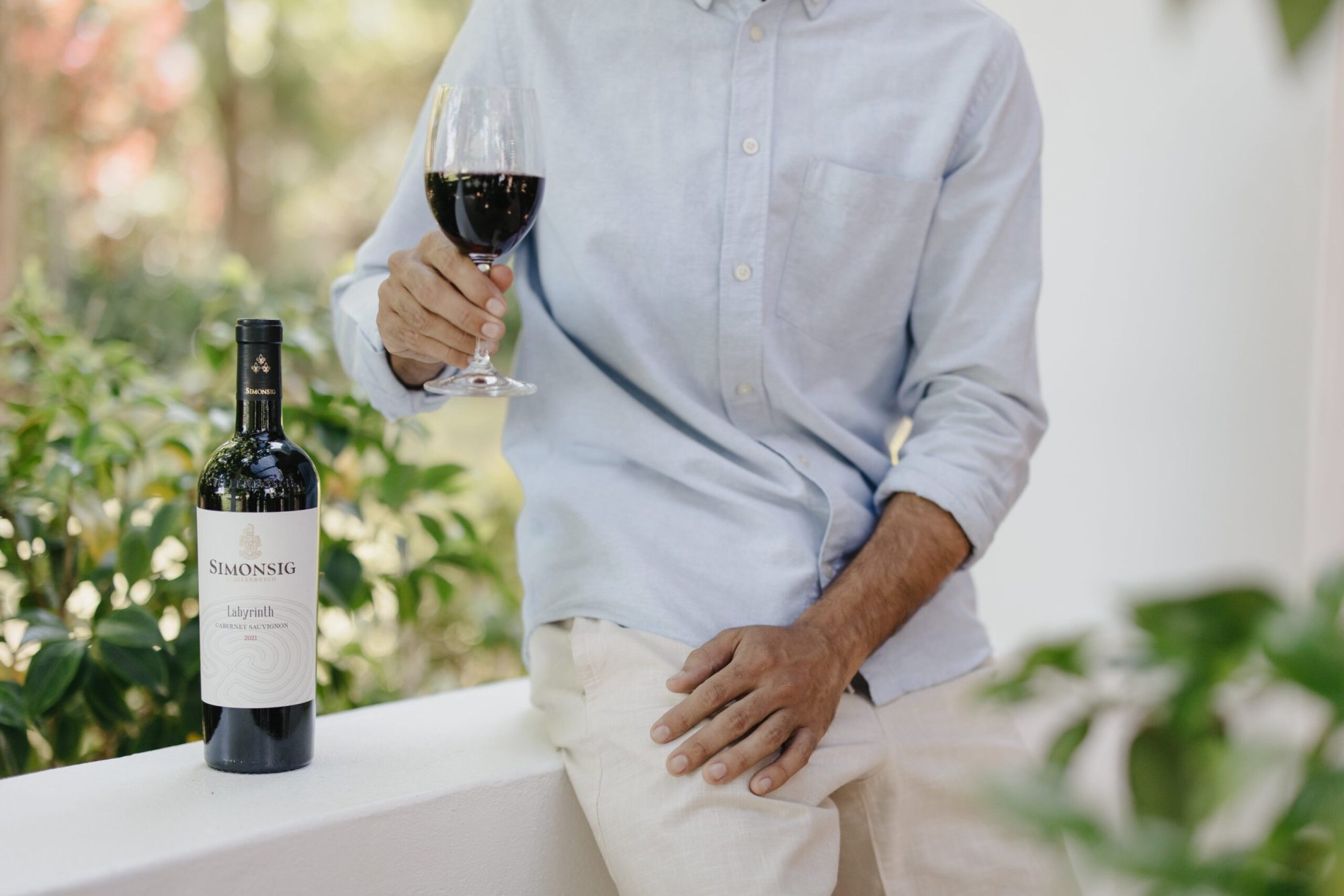 Person holding a glass of red wine beside a bottle of Simonsig wine