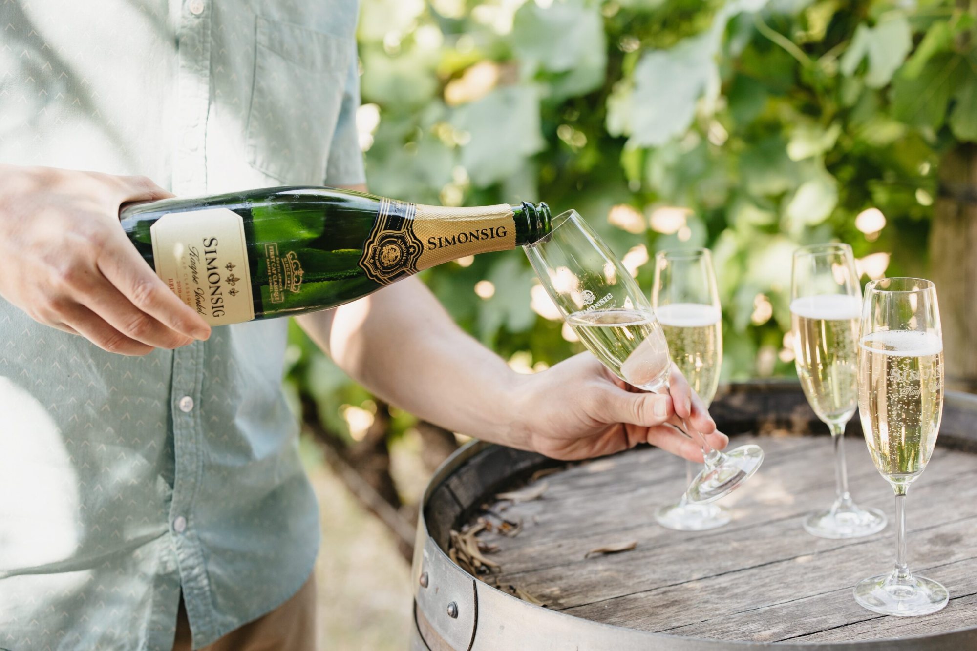 A person pouring Kaapse Vonkel sparkling wine into glasses.