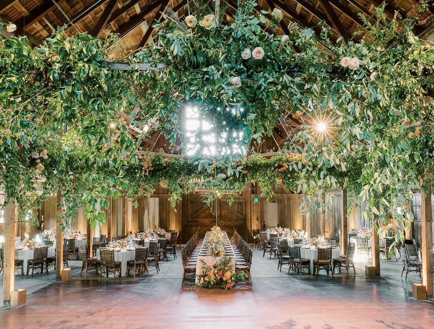 Indoor wedding venue with long tables and hanging greenery.